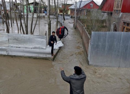 A man throws his belongings towards another to be moved to a safer place at a flooded neighbourhood after incessant rains in Srinagar March 30, 2015. REUTERS