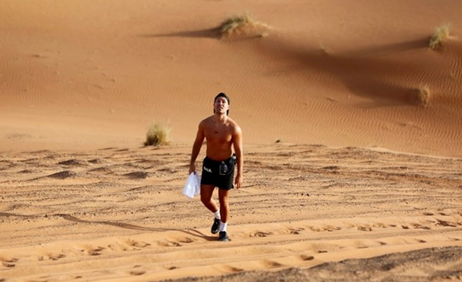Man lowers himself into ice tub as sun bakes orange dunes of UAE desert